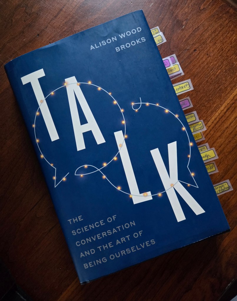 Cover of the book 'TALK: The Science of Conversation and the Art of Being Ourselves' by Alison Wood Brooks, featuring a blue background and light designs around the word 'TALK'.